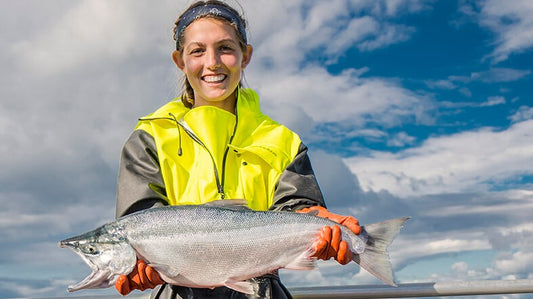 Young woman holding a salmon with blue sky with clouds behind her.
