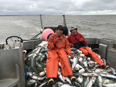 Two Alaskan fisherman sit on a gillnet full of salmon on their commercial fishing boat